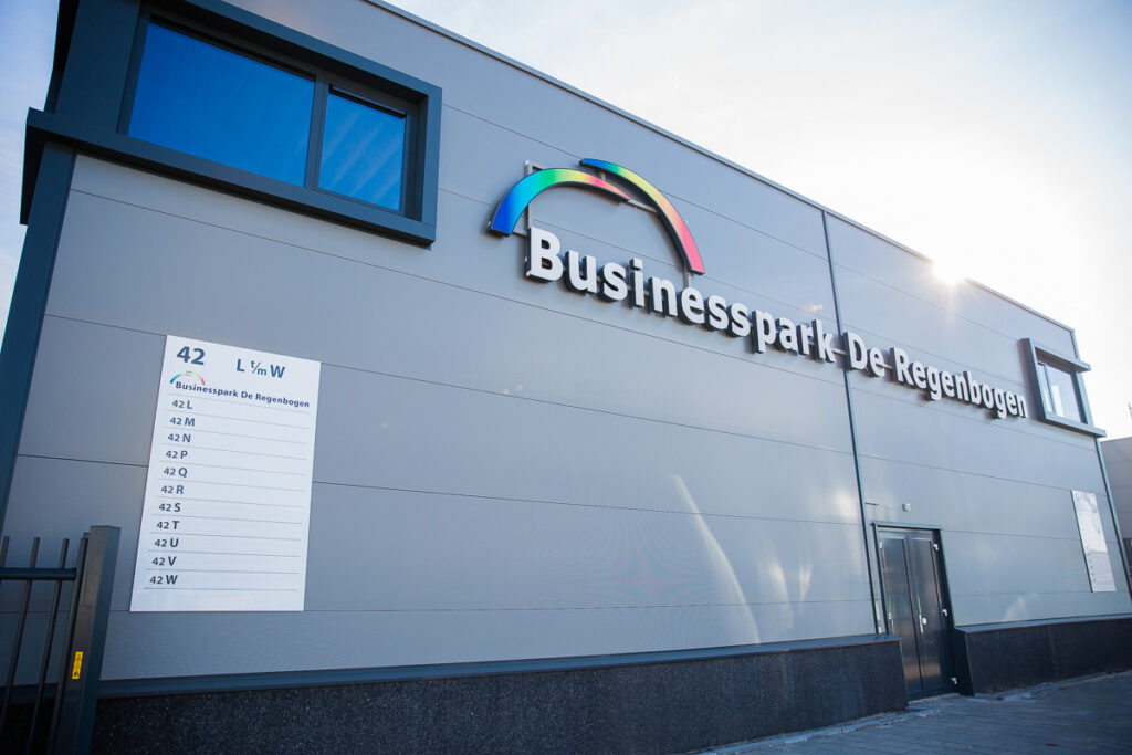 Grijze gevel van Businesspark De Regenbogen aan de Laan van ‘s-Gravenmade met kleurrijk logo en overzichtsbord van units.